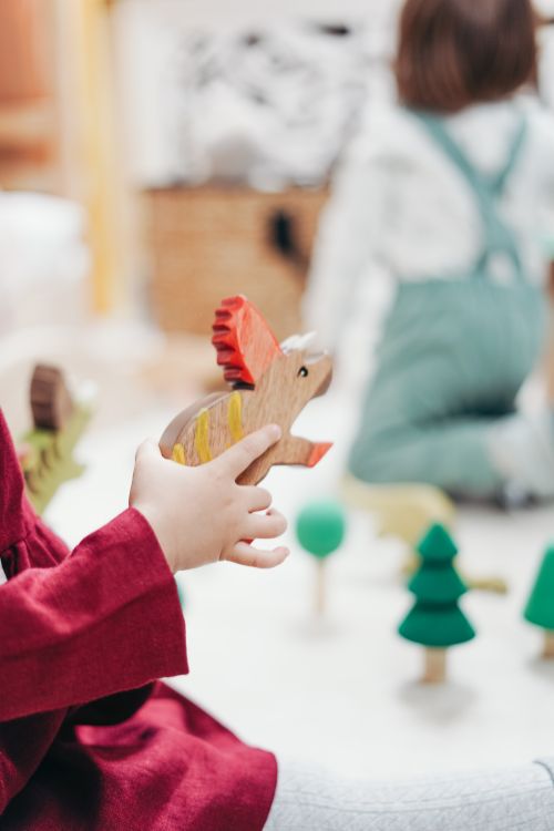 Free A child playing indoors with a colorful wooden dinosaur toy, creating a fun and imaginative playtime environment. Stock Photo