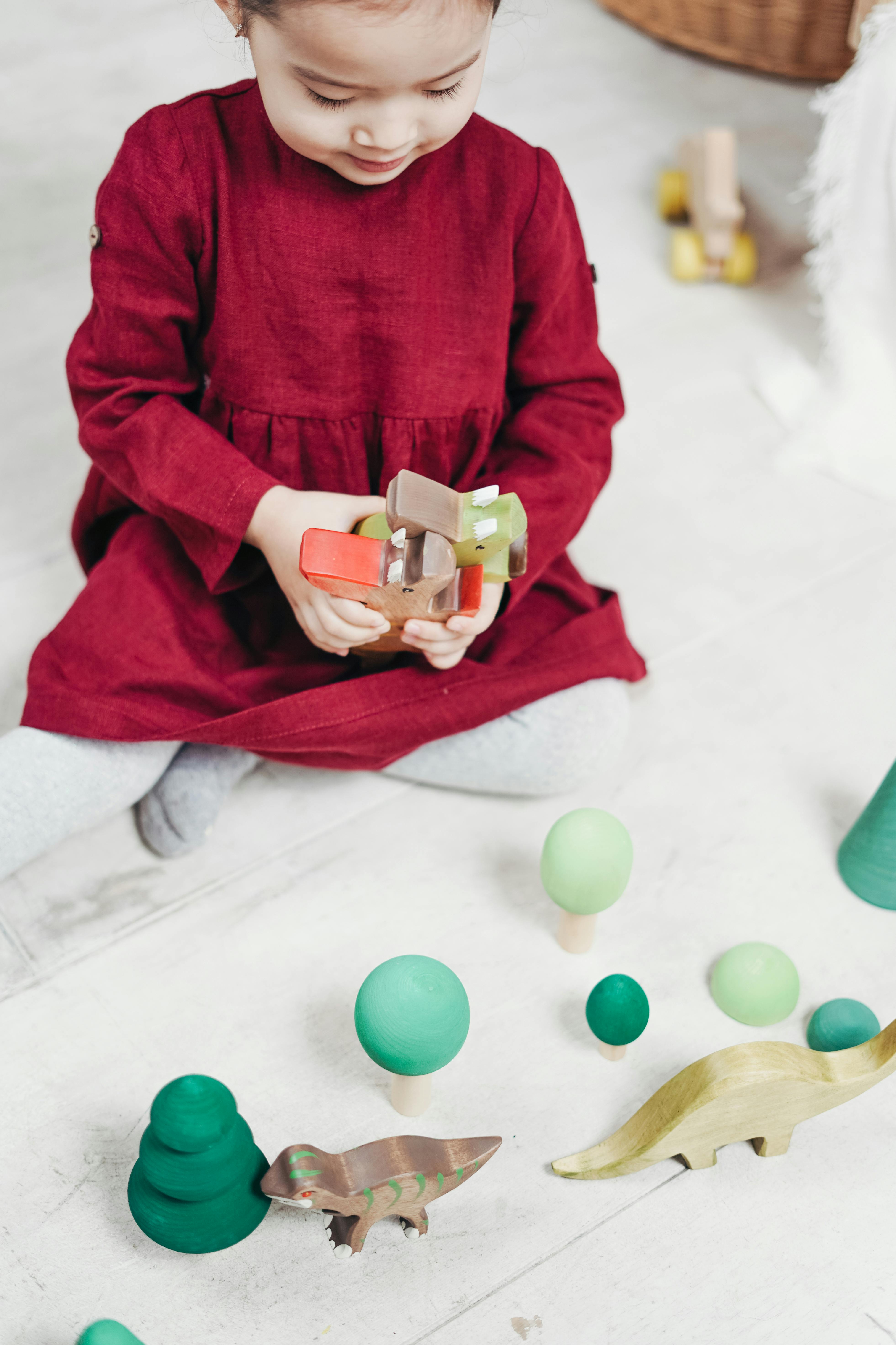 girl in red long sleeve dress sitting on white floor tiles playing with toys