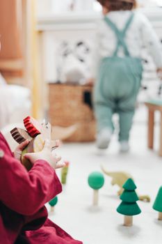 Two children engaged in play with wooden toys in bright indoor setting.