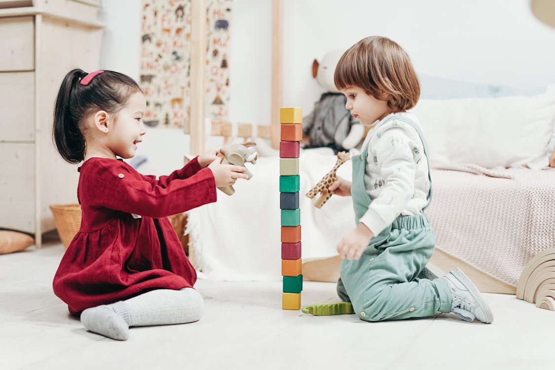 白の長袖シャツと赤の女の子の横に床に座っている緑のズボンの男の子