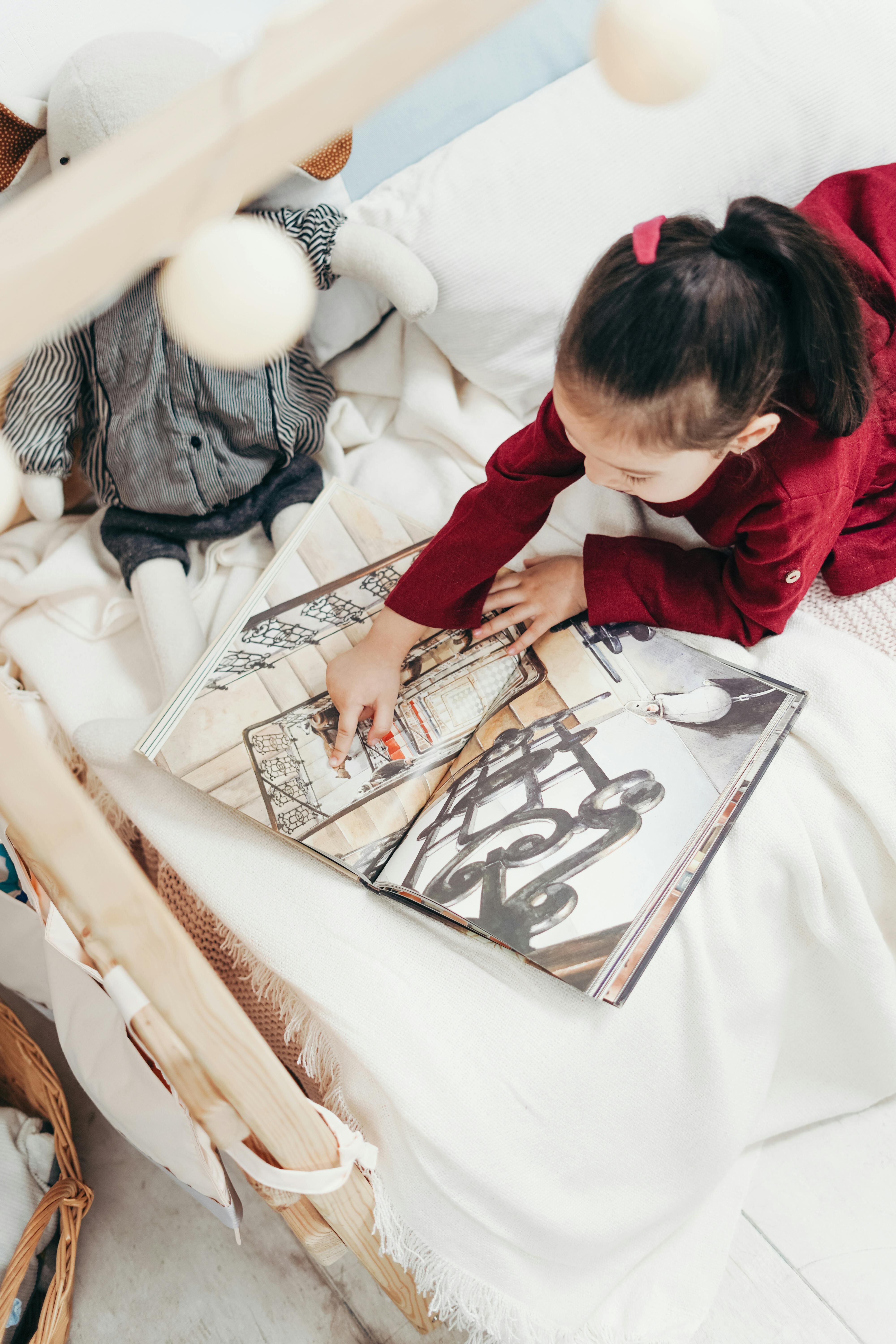 Cute child reading on a bed surrounded by soft toys. Indoors, cozy reading time.