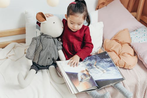 Girl in Red Dress Sitting on Bed Reading Book