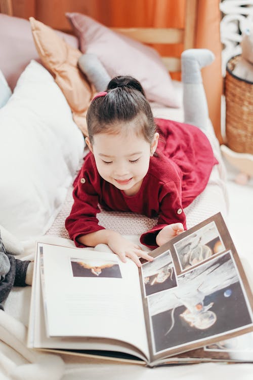 Free Girl in Red Dress Lying in Bed Reading Book Stock Photo