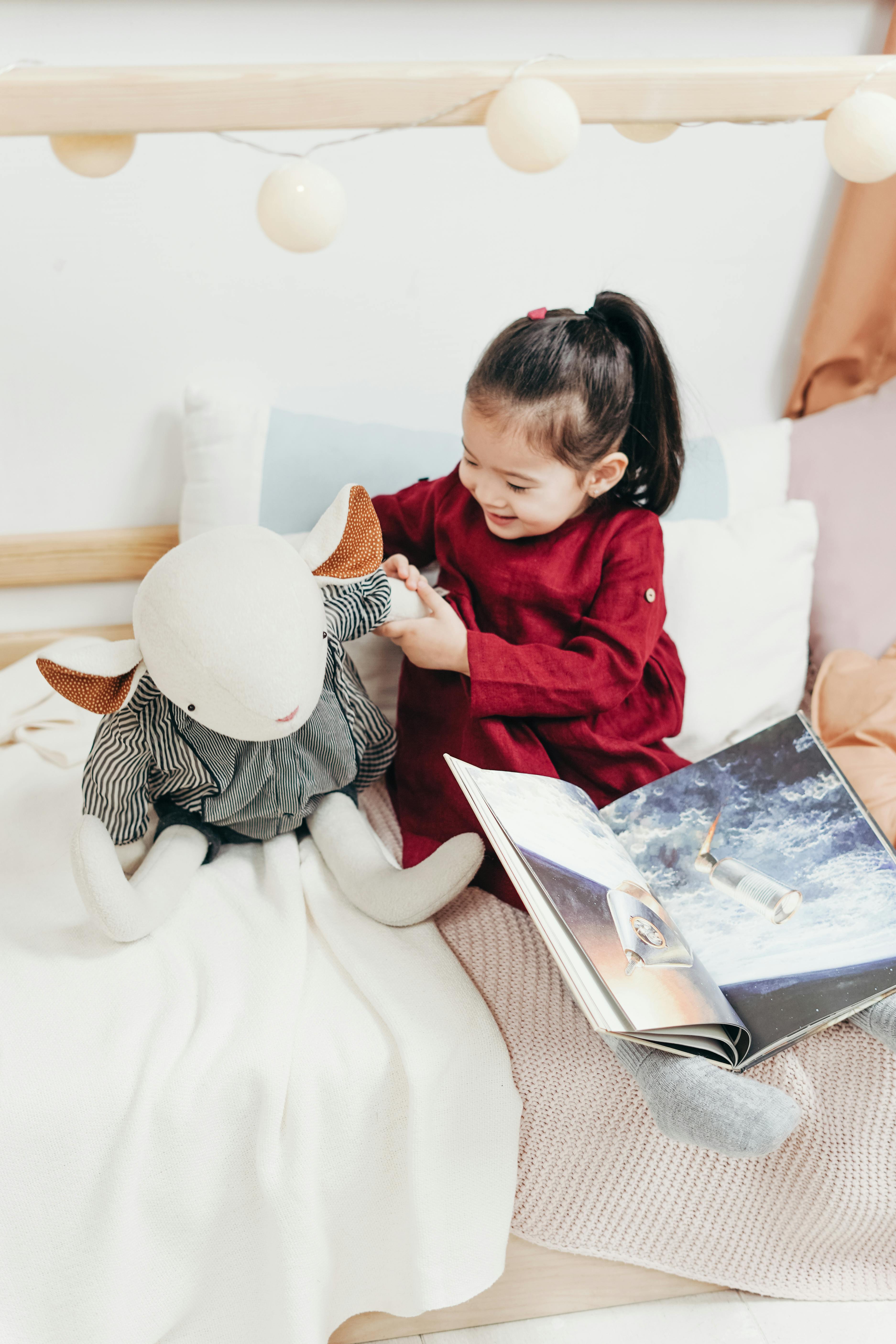 可爱的亚洲女孩坐在室内的床上，开心地玩着毛绒玩具