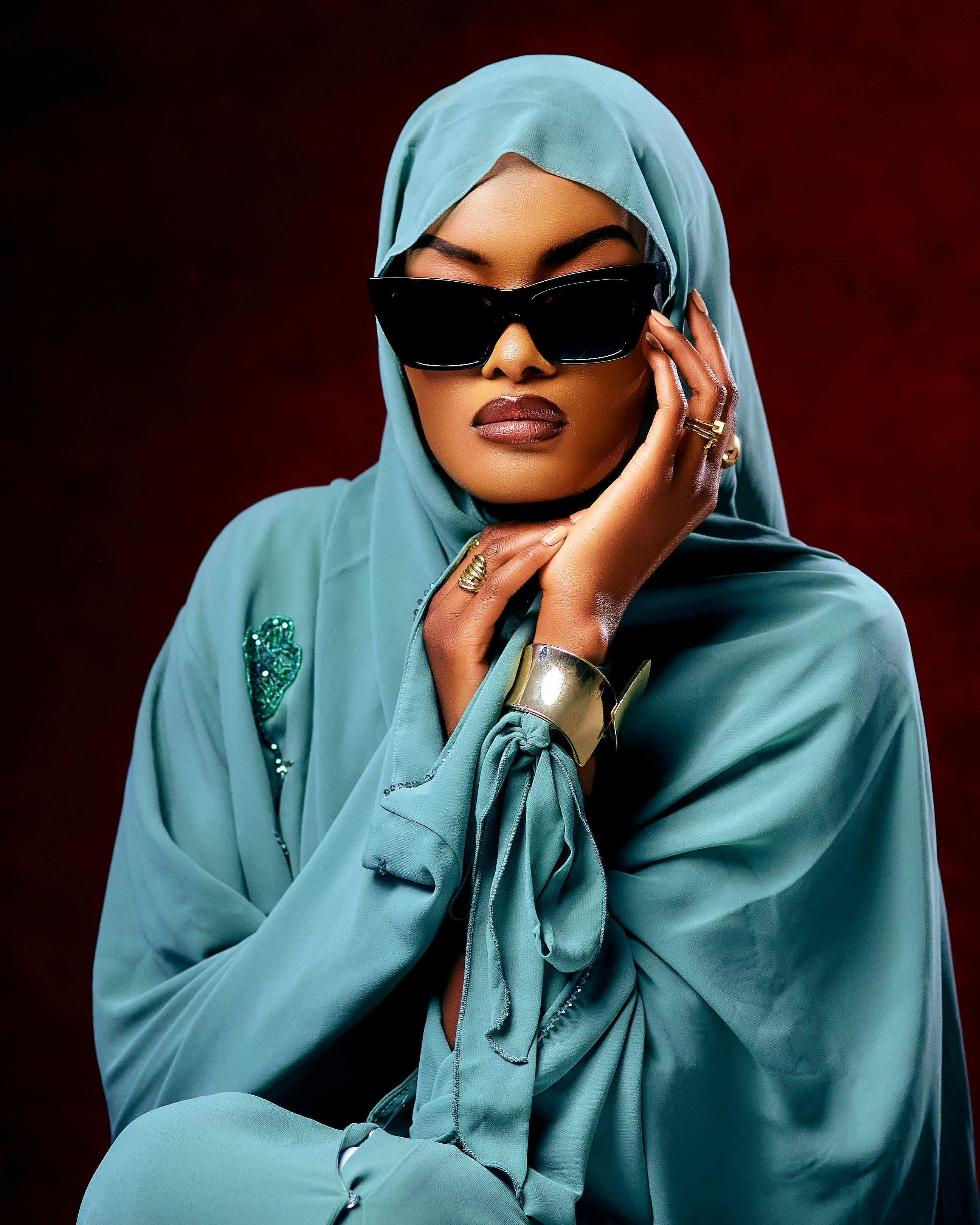 Elegant woman wearing hijab, sunglasses, and jewelry posing with confidence.