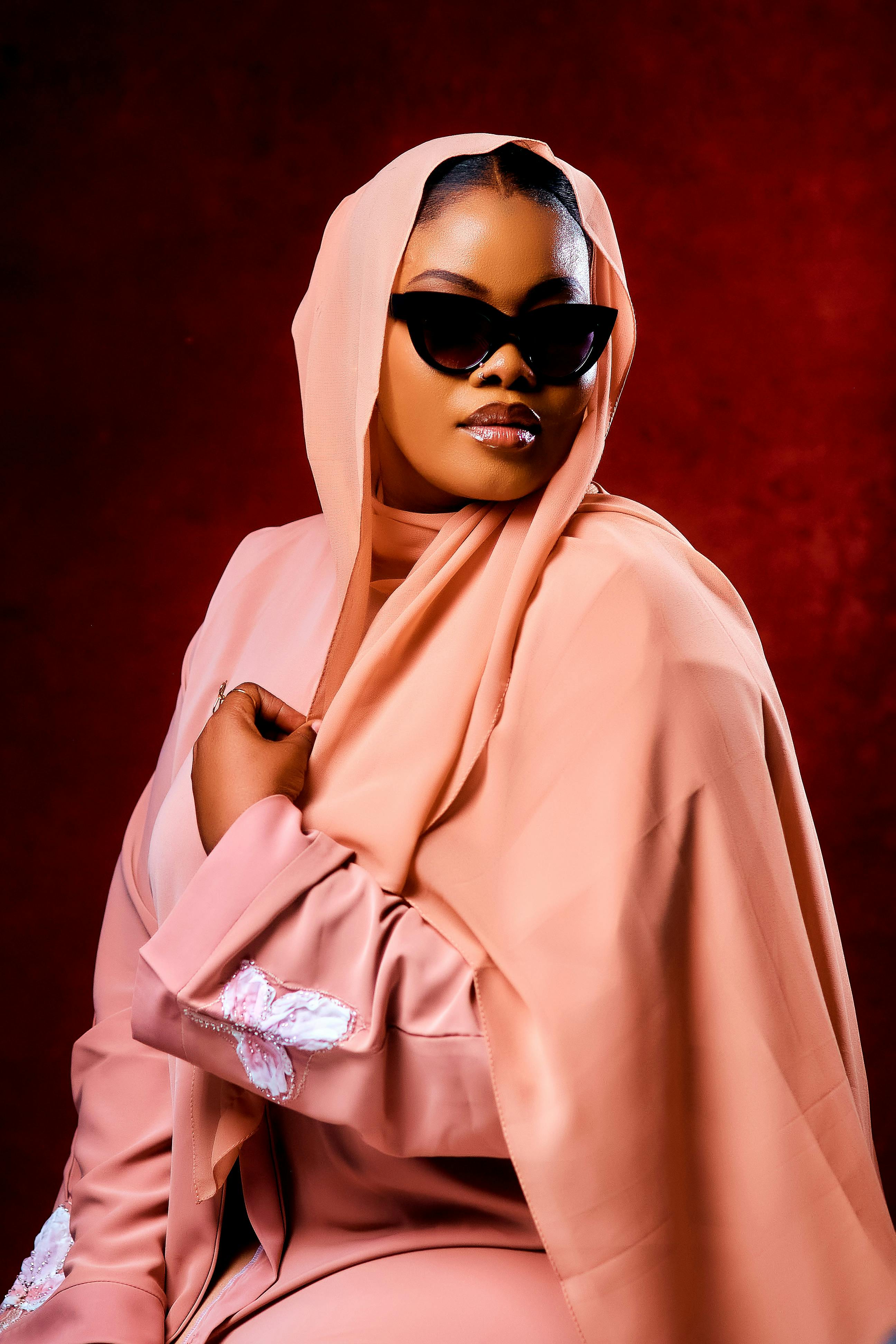 Zadarmo Štýlová žena v broskyňovom hidžábe a slnečných okuliaroch na tmavočervenom pozadí. Fotka z fotobanky