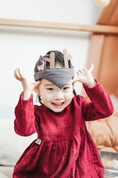 一个可爱的亚洲女孩穿着红色连衣裙，戴着玩具王冠，在室内微笑着玩耍