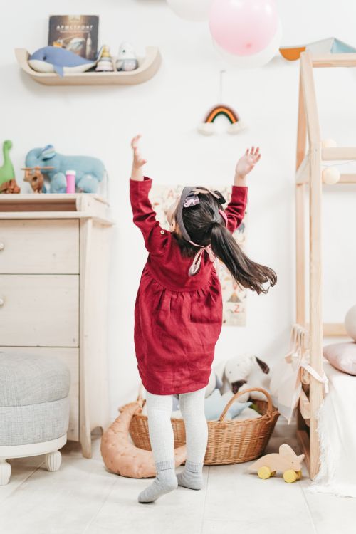 Free A young girl in a red dress jumps to catch balloons in a cozy bedroom setting. Stock Photo