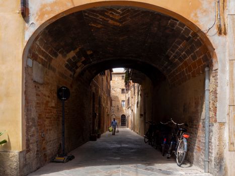 Rustic alleyway under an ancient arch with a cyclist in Buonconvento, Tuscany.