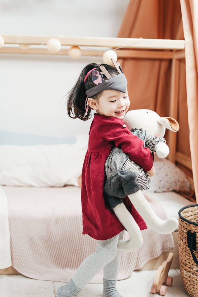 Smiling Girl In Red Dress Carrying Doll