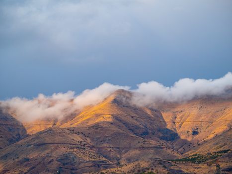 Breathtaking view of mountains with clouds and sunlight casting golden hues, capturing the serene natural beauty.