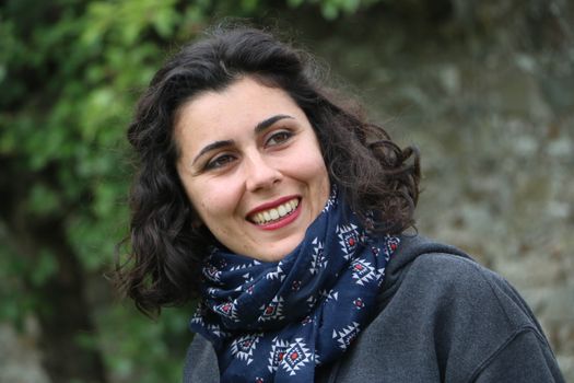 Smiling woman with curly hair wearing a patterned blue scarf outdoors.
