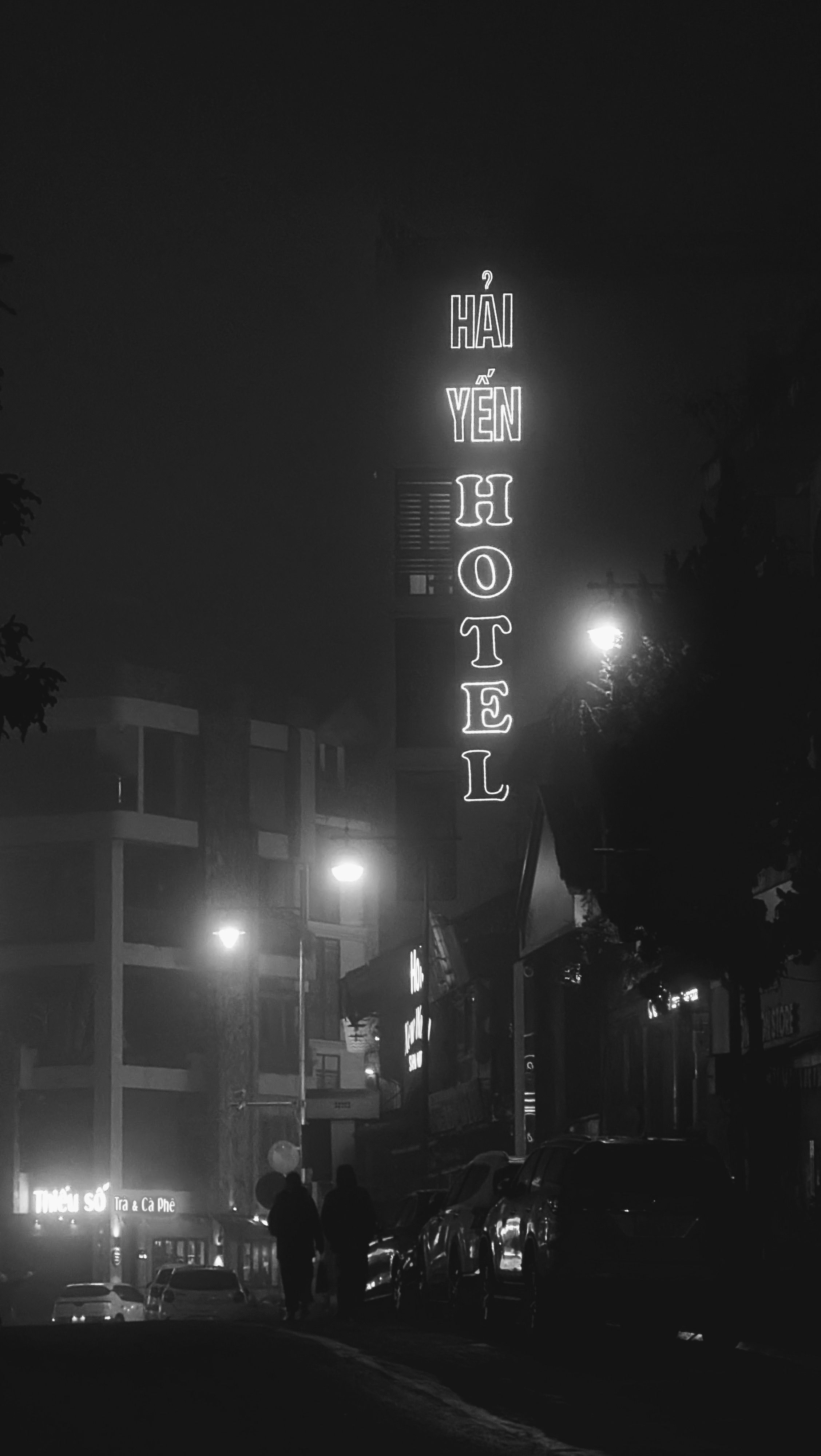 A moody black and white street view of Hai Yen Hotel in Lao Cai, Vietnam on a misty night.
