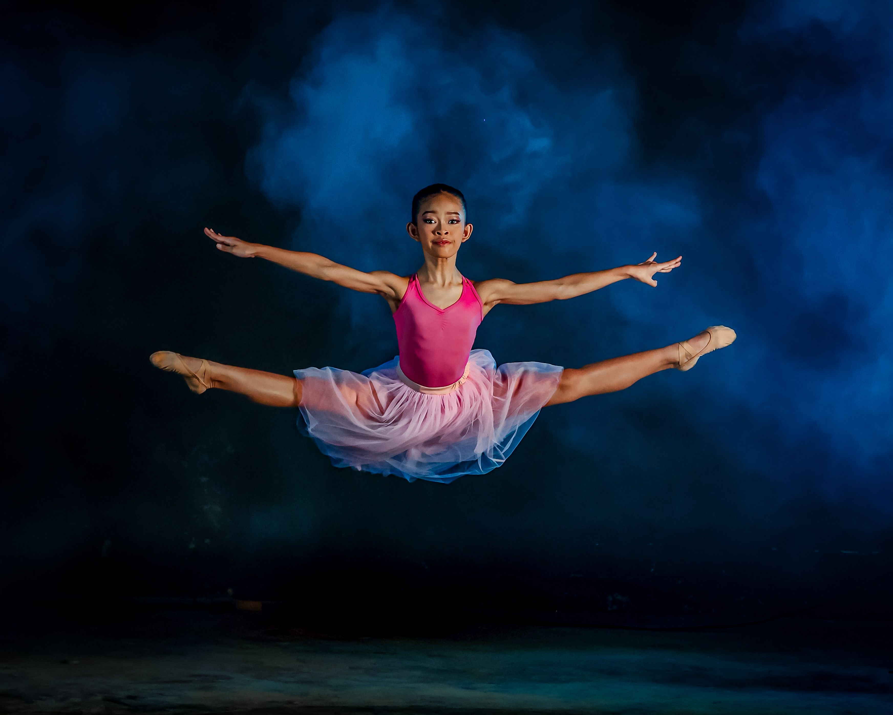 Graceful ballerina in a pink tutu executing a perfect leap against a dramatic backdrop.
