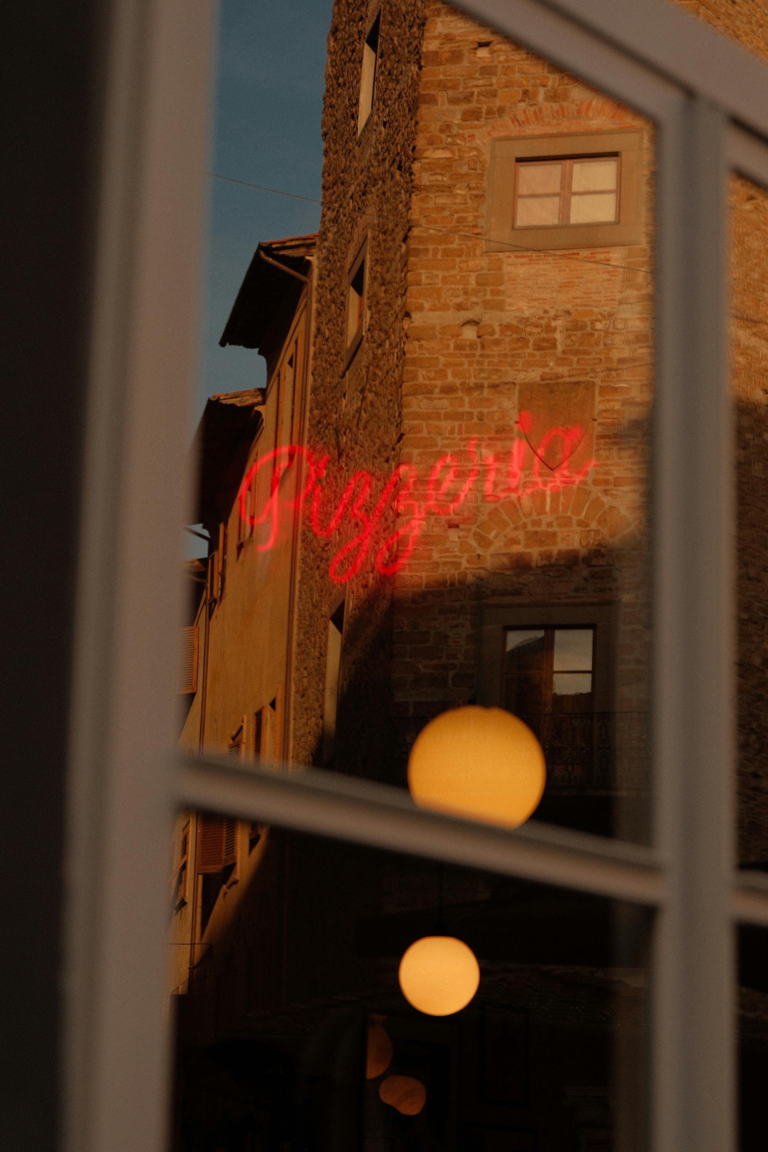 Reflection of a red neon pizzeria sign on a rustic building with warm evening tones.