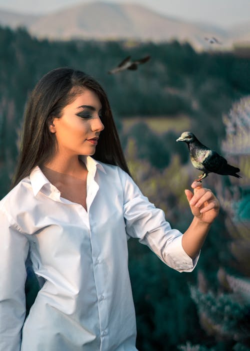 Free Young woman with bird on hand in woodland Stock Photo