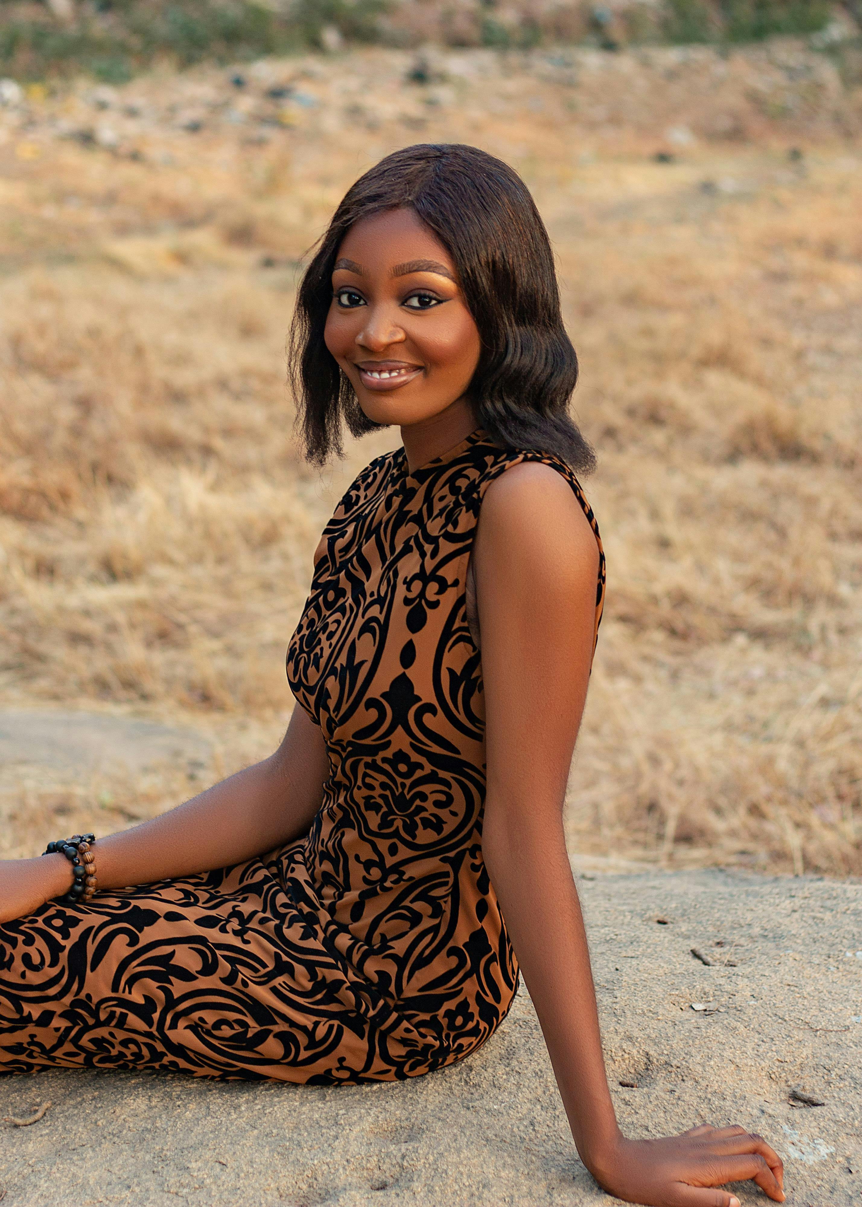 Zadarmo Žena sediaca vonku s úsmevom vo vzorovaných šatách pod prirodzeným svetlom. Fotka z fotobanky