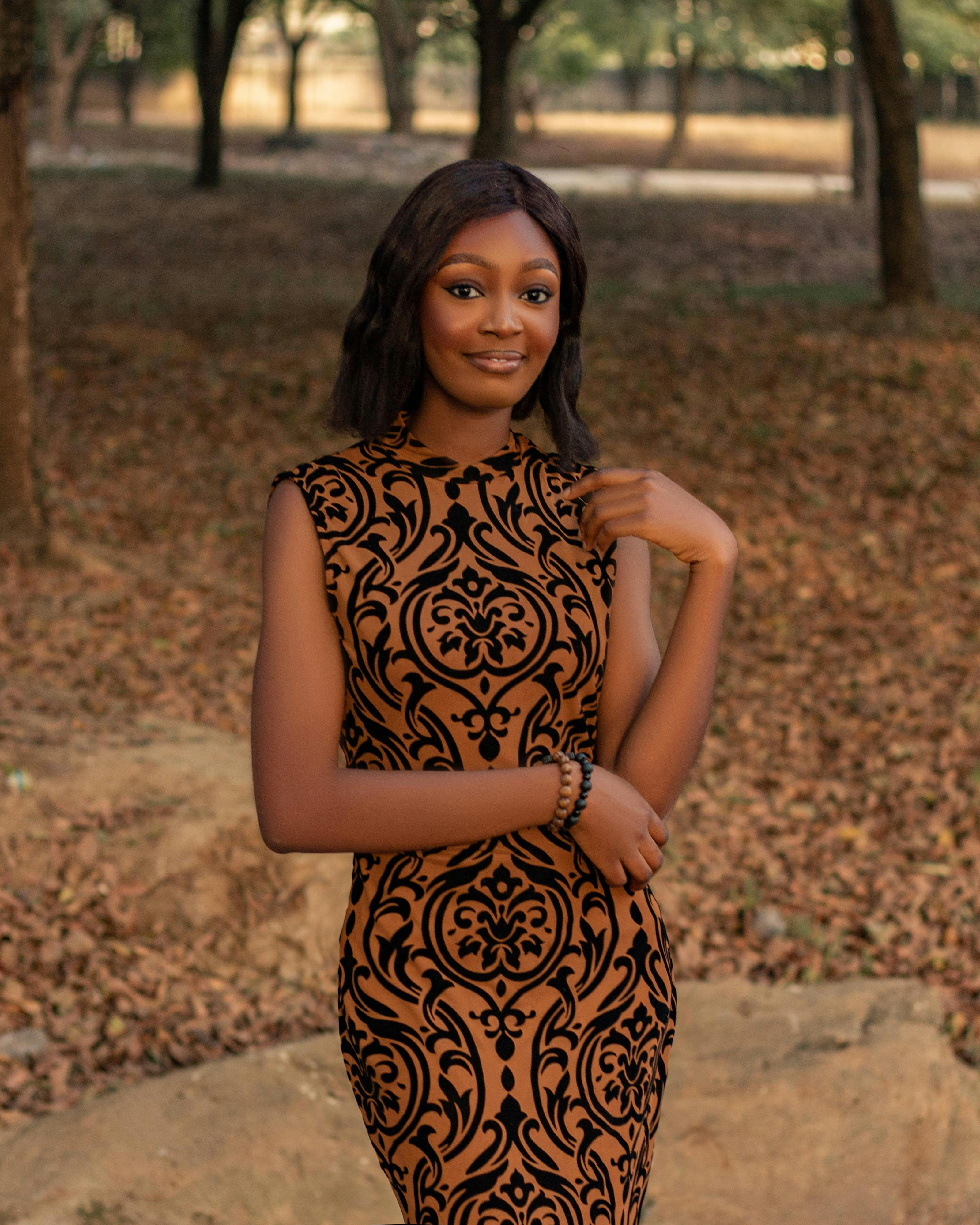 Безкоштовне Стильна жінка позує у візерунчастій сукні на тлі осіннього лісу. стокове фото