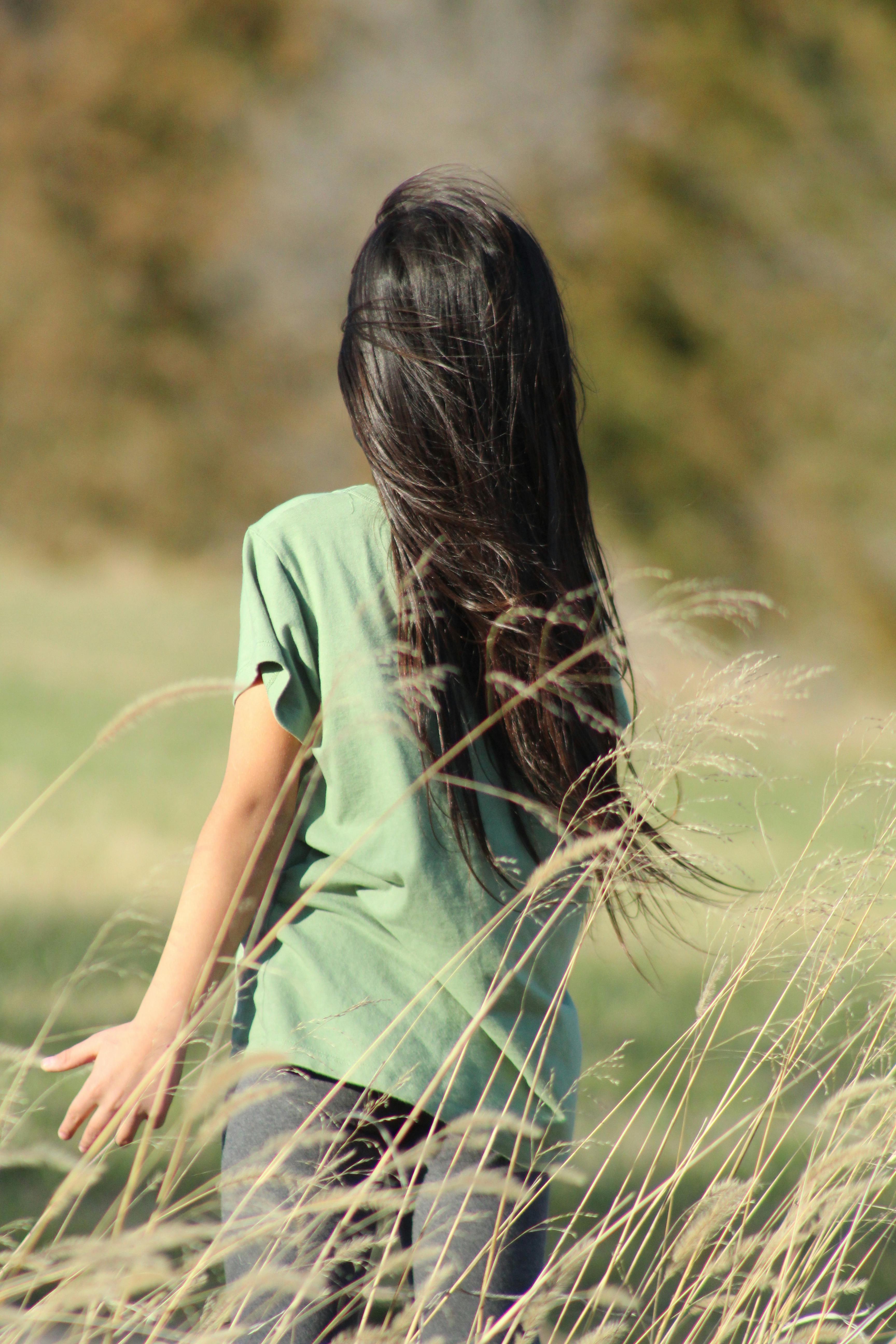 免費 一個長髮少女背對著鏡頭，走過一片高高的草叢。 圖庫相片