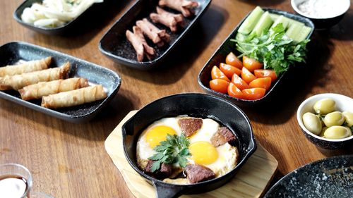 Free Appetizing breakfast spread with eggs, vegetables, olives, and spring rolls on a wooden table. Stock Photo