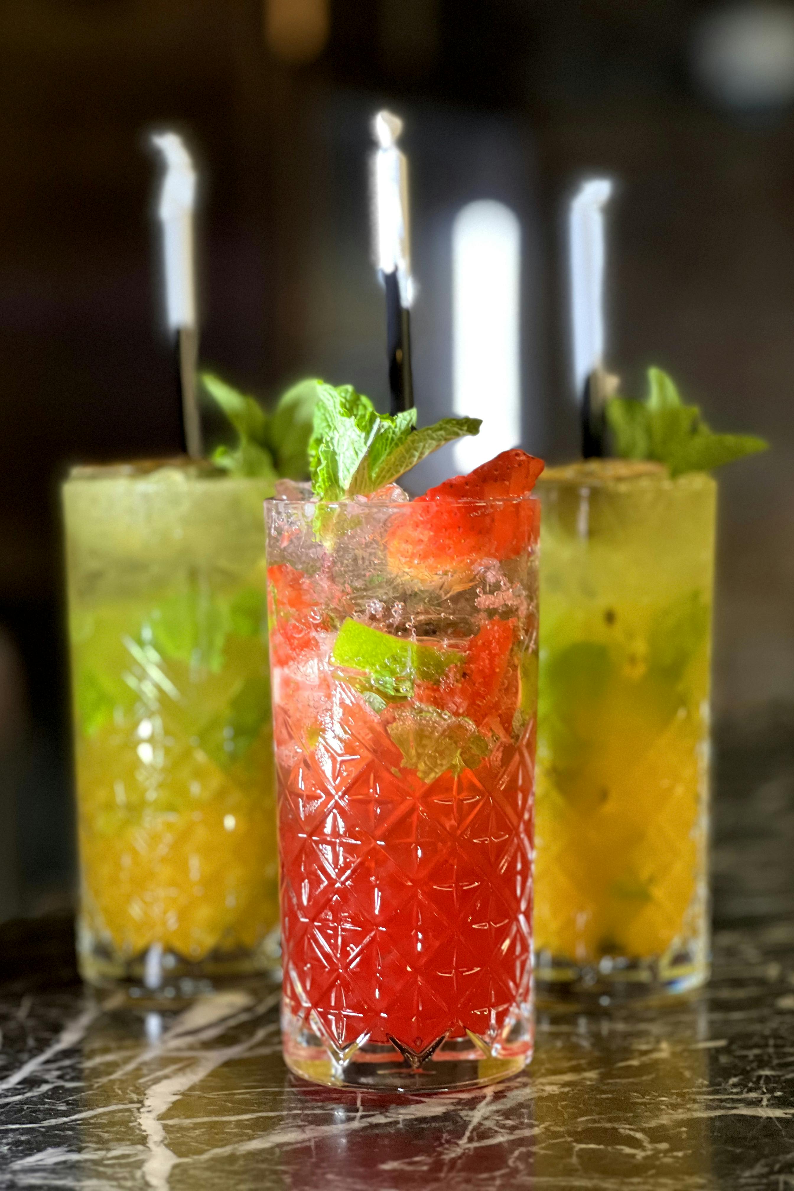 免費 三杯色彩繽紛的雞尾酒，以薄荷葉、青檸和水果裝飾，盛放在大理石檯面上。 圖庫相片