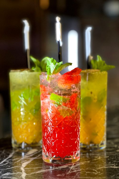 Free Three colorful cocktails with mint, lime, and fruit garnishes on a marble surface. Stock Photo