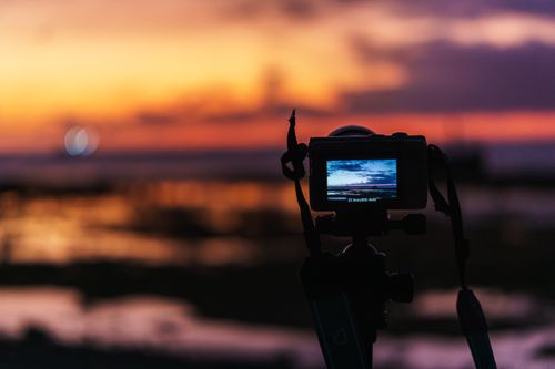 Free A serene beach sunset captured on a camera tripod, showcasing vivid colors. Stock Photo