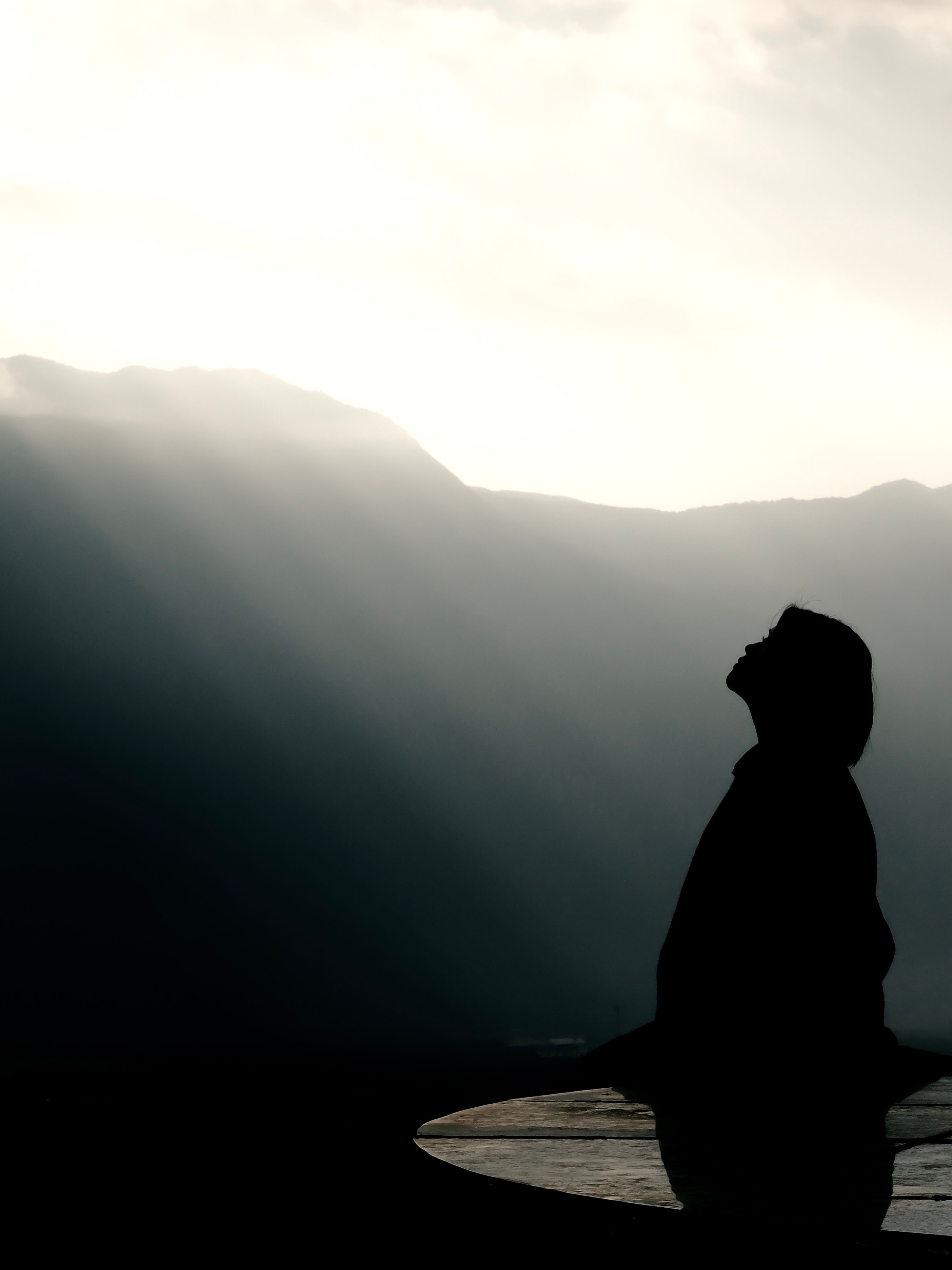 A person silhouetted against a sunrise, standing near mountains, conveying a sense of peace and contemplation.