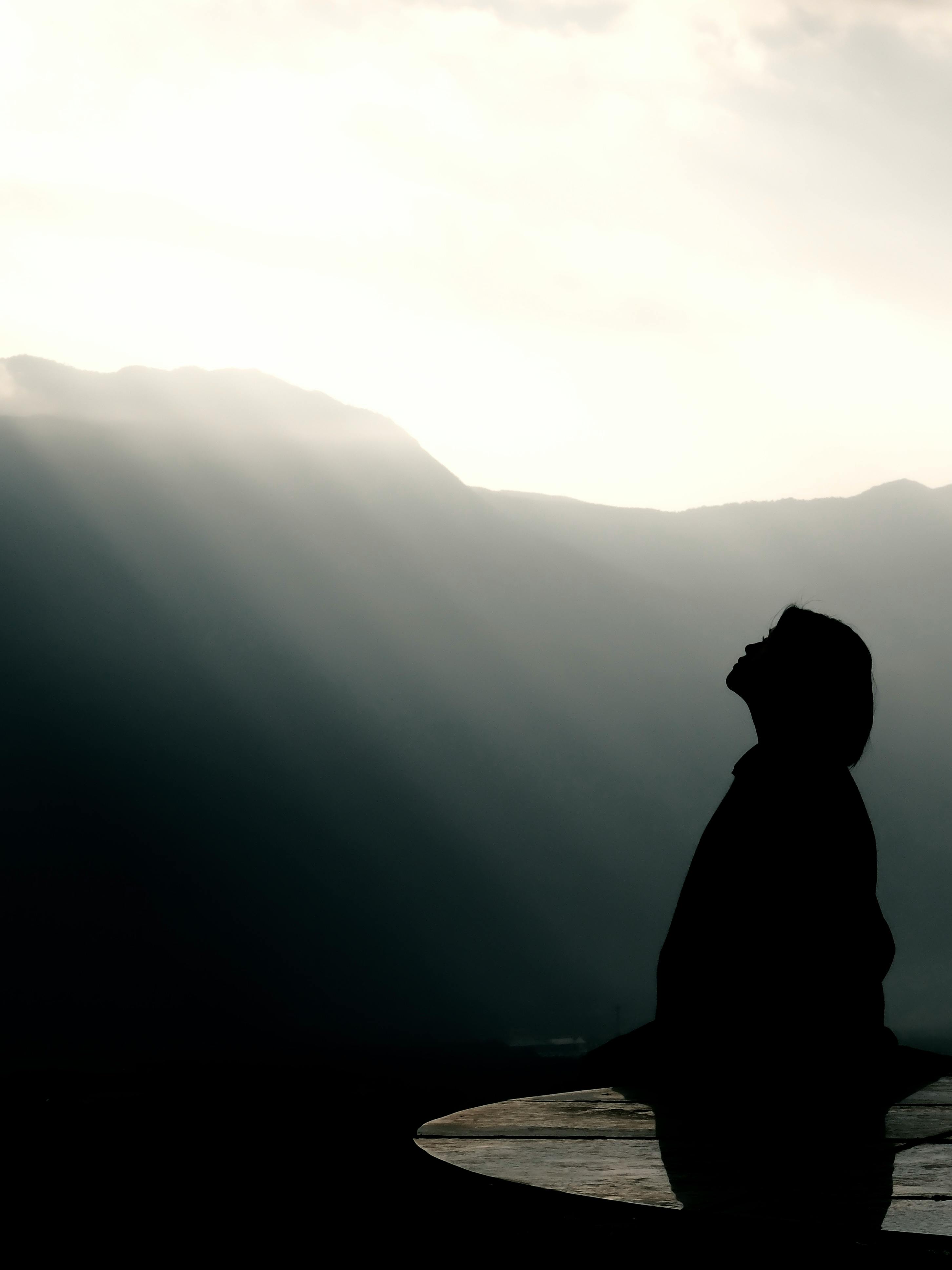 ingyenes Egy személy sziluettje a napfelkelte előtt, hegyek közelében áll, békét és elmélkedést sugározva. Stockfotó