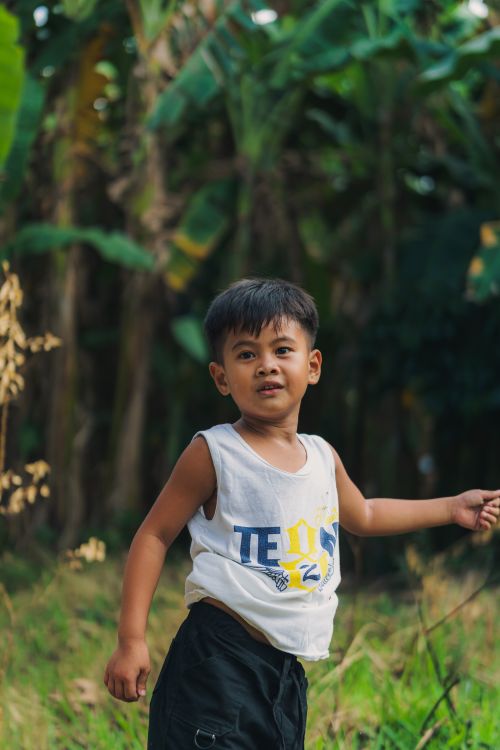 Free A young boy enjoying a playful moment in a forest setting with lush greenery around. Stock Photo