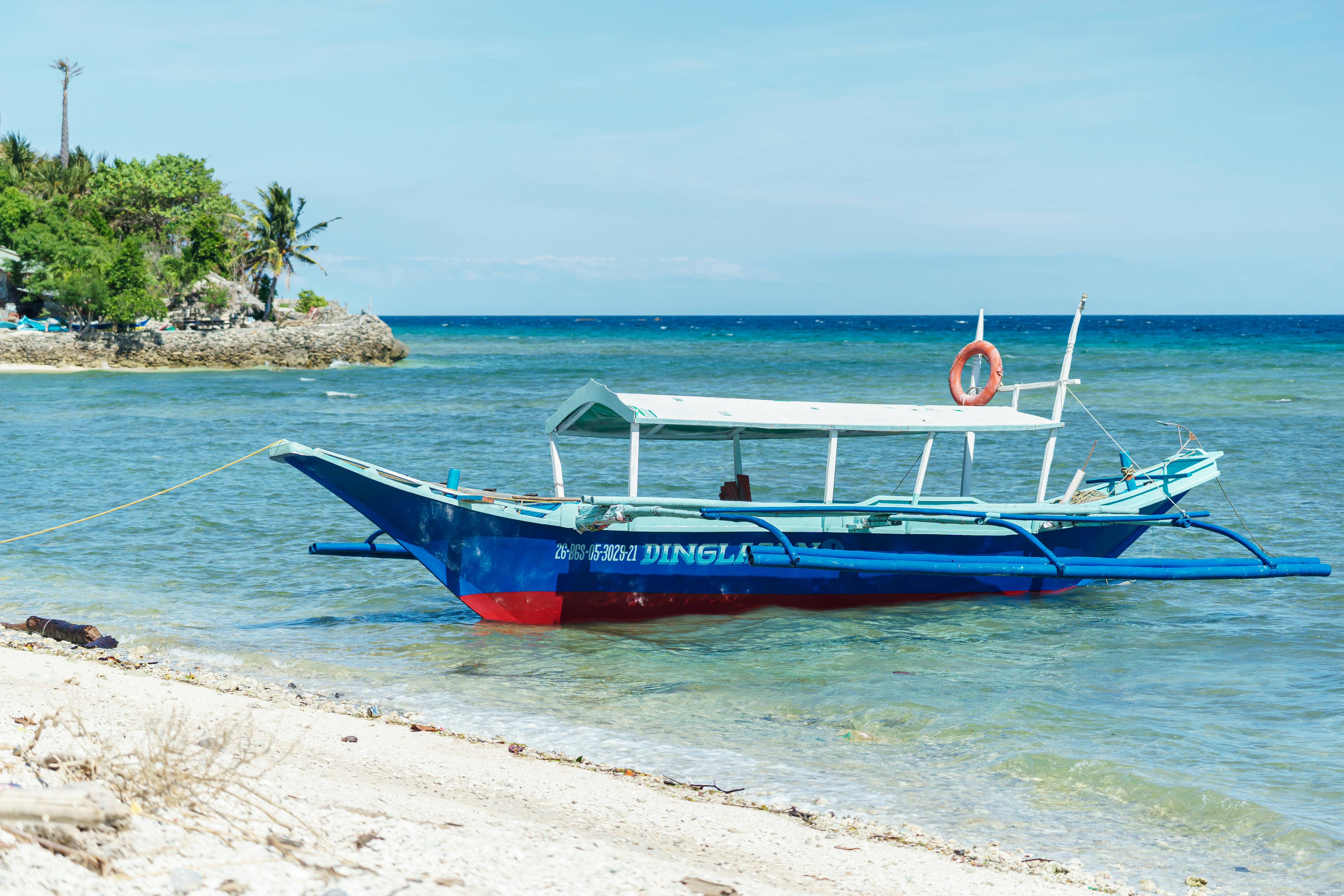 ฟรี เรือสีฟ้าสดใสจอดอยู่บนหาดทรายขาวสะอาดในเขตร้อนชื้น ภายใต้ท้องฟ้าแจ่มใส มอบทัศนียภาพชายฝั่งอันเงียบสงบ คลังภาพถ่าย