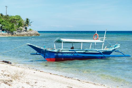 Free A vibrant blue boat rests on a clear tropical beach under a sunny sky, offering a serene coastal view. Stock Photo