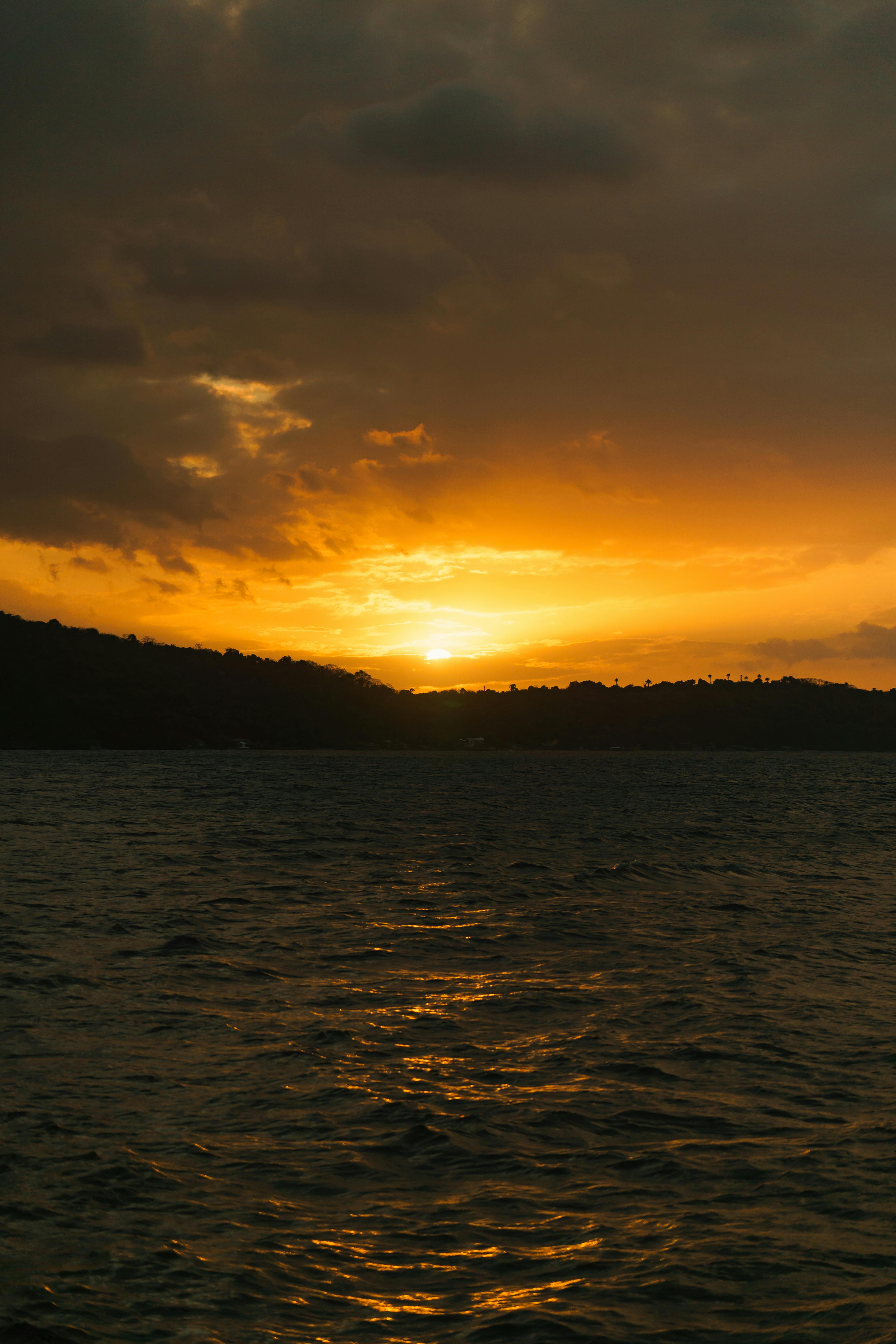 ฟรี ภาพพระอาทิตย์ตกดินอันงดงามด้วยสีส้มสดใสเหนือผืนน้ำอันสงบนิ่ง สะท้อนแสงและมอบความสงบสุข คลังภาพถ่าย