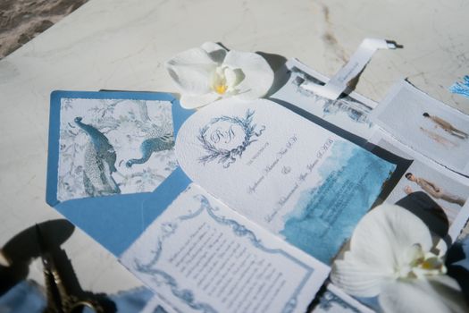Elegant wedding invitation set featuring peacock design and white orchids on a marble background.