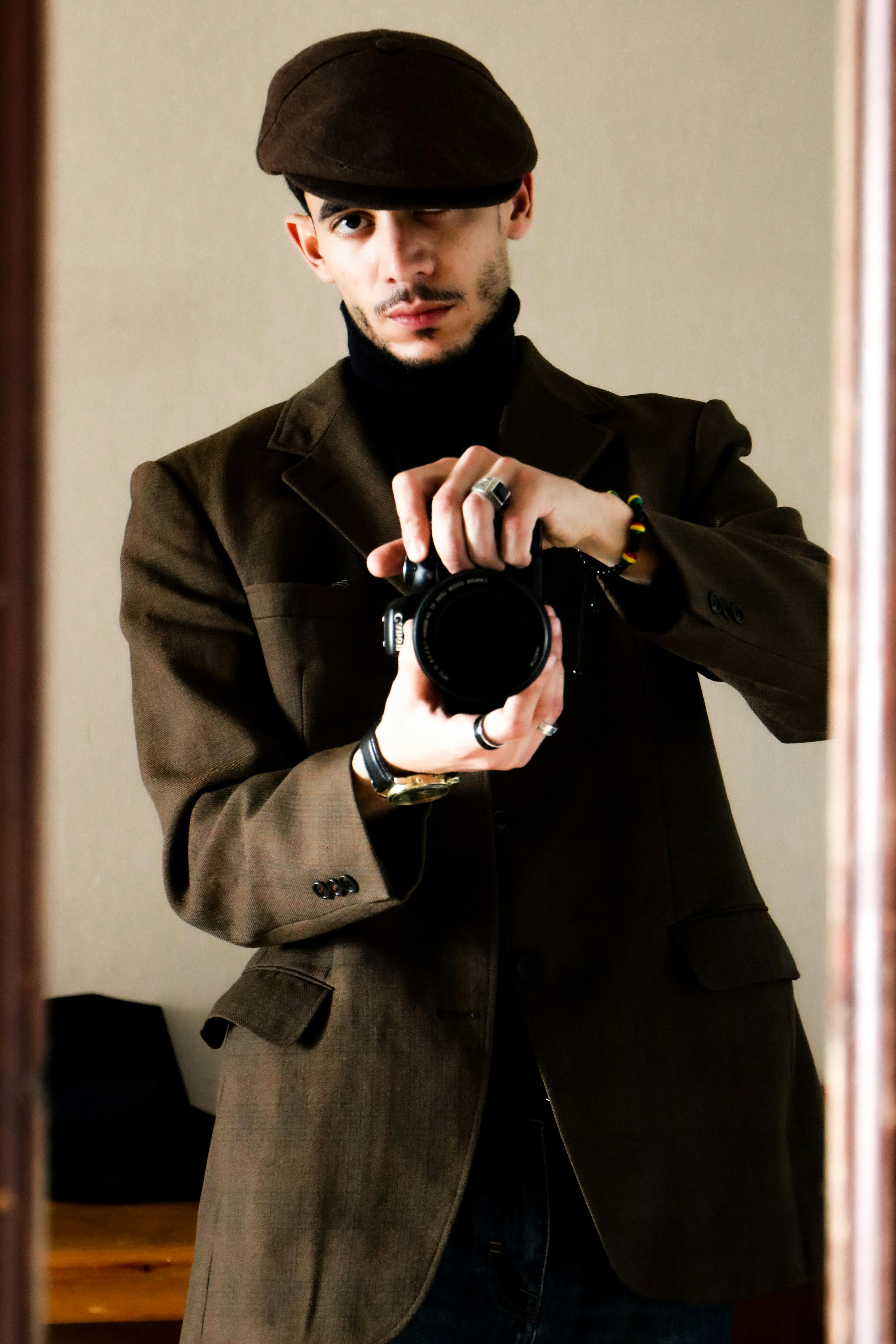 Man in brown blazer and hat taking a mirror selfie, showcasing modern fashion.