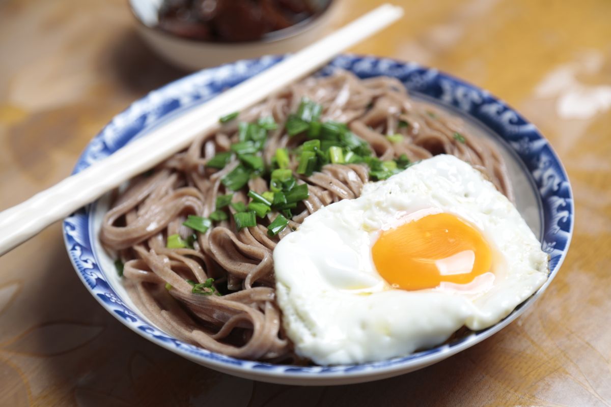 Brown soba noodles with chopped scallions and a sunny-side-up fried egg in a blue-rimmed bowl