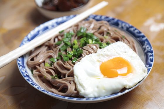 Brown soba noodles with chopped scallions and a sunny-side-up fried egg in a blue-rimmed bowl