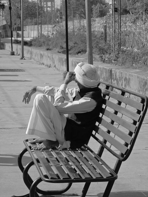 Free A senior man in traditional Indian clothing relaxes on a bench in an outdoor setting, captured in black and white. Stock Photo