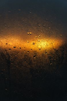 Warm sunset light filtered through a rain-splattered window, creating an abstract, moody scene.