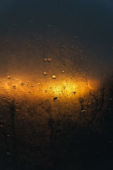 Abstract view of raindrops on a window reflecting the warm glow of sunset light.