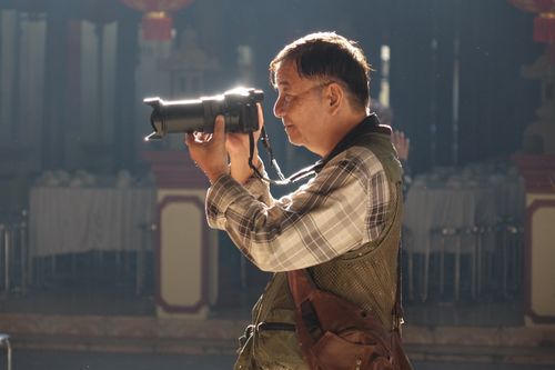 Free An elderly man taking photos indoors with a DSLR camera, highlighting passion for photography. Stock Photo