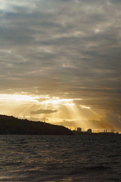 Free Golden sunset rays streaming through clouds over the ocean, creating a dramatic and serene landscape. Stock Photo