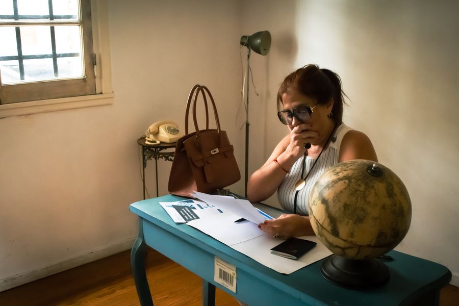A woman focuses on paperwork at a desk with a globe and vintage phone.