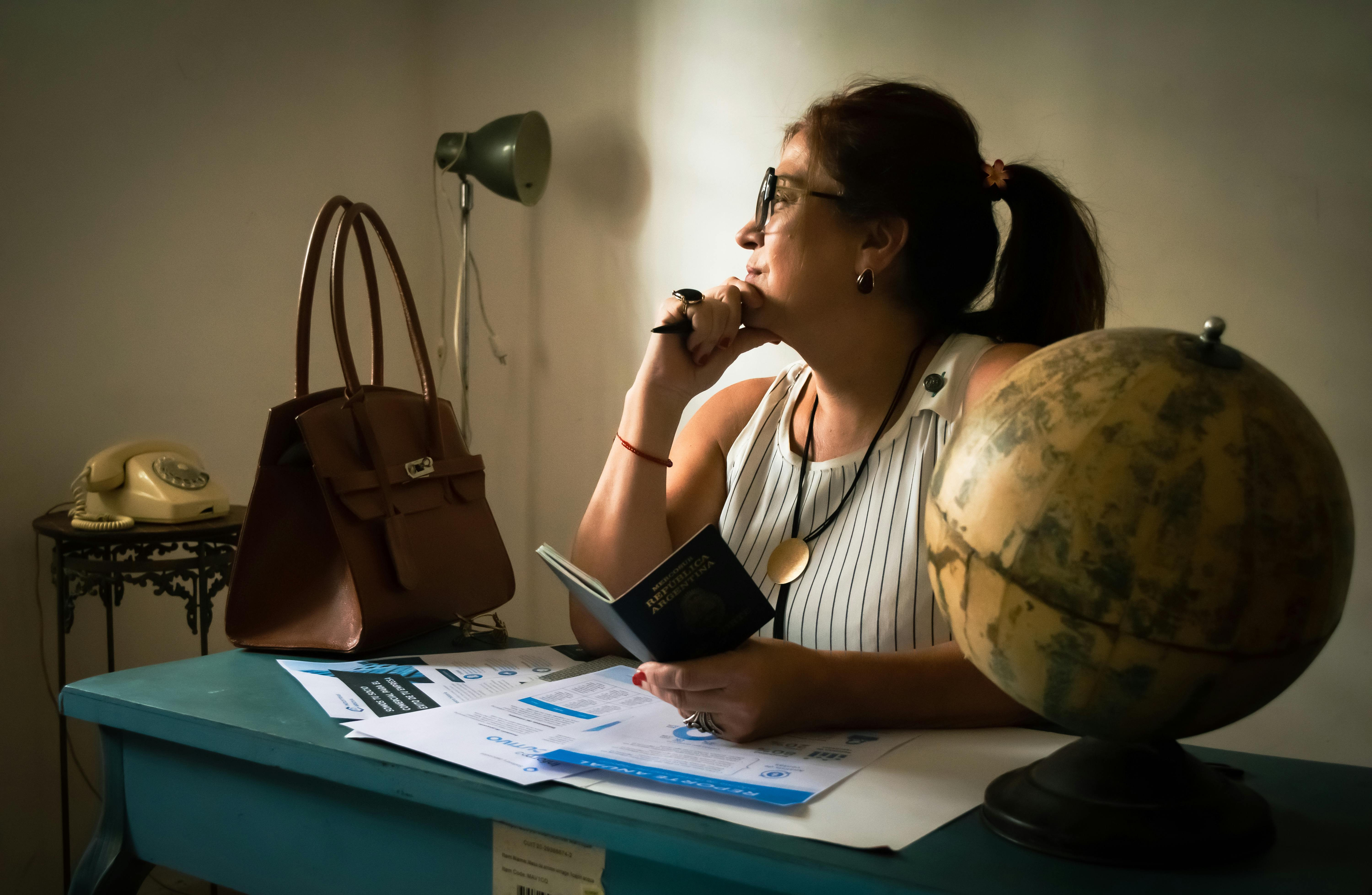 ingyenes Üzletasszony töpreng az íróasztalánál egy földgömbbel, dokumentumokkal és egy lámpával. Intellektuális hangulatot ragad meg. Stockfotó