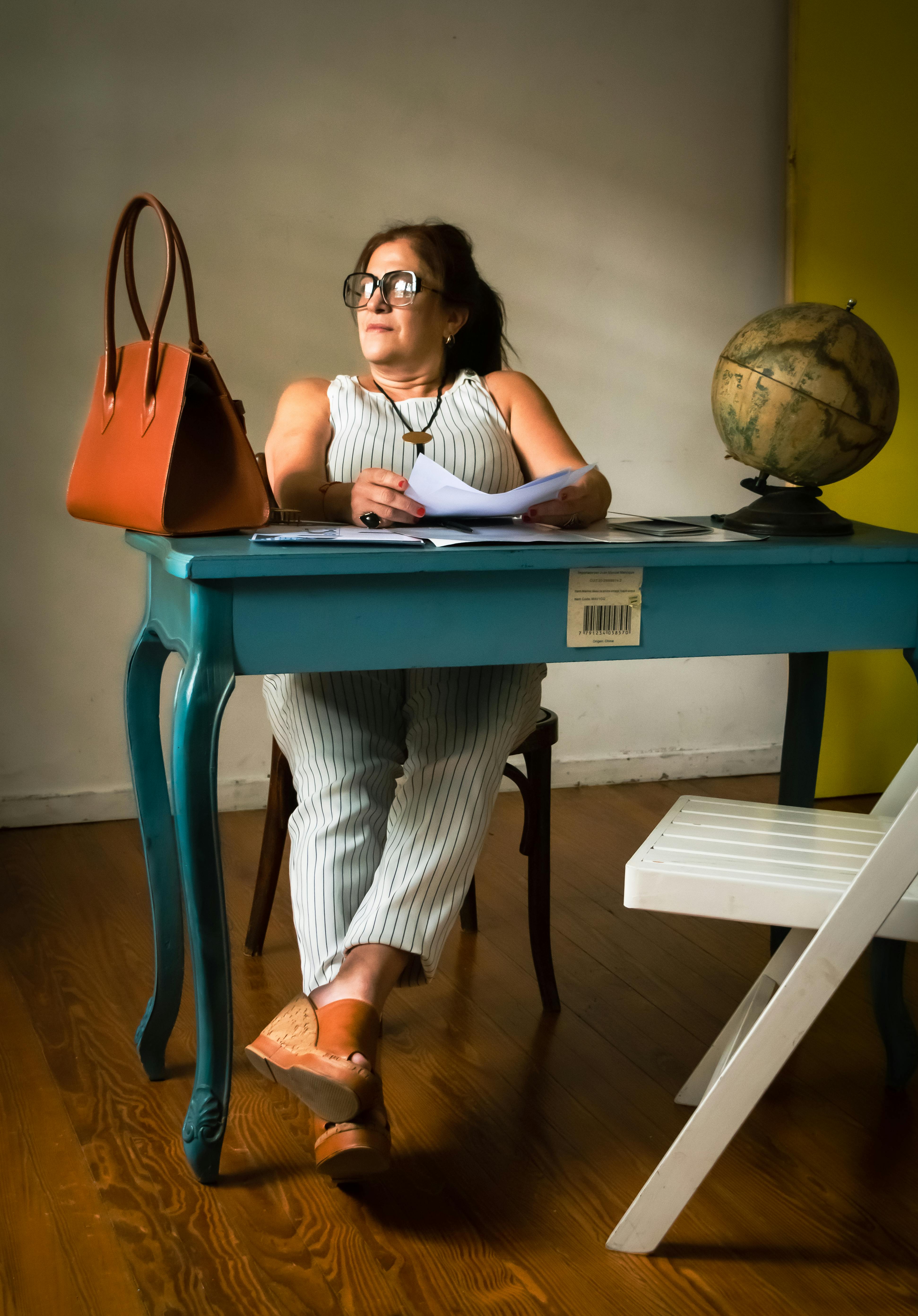 ฟรี หญิงสาวนั่งอยู่ที่โต๊ะสีฟ้าในห้องทำงานที่บ้าน โดยมีลูกโลกและกระเป๋าถือวางอยู่ข้างๆ เธอกำลังครุ่นคิดถึงเรื่องงาน คลังภาพถ่าย