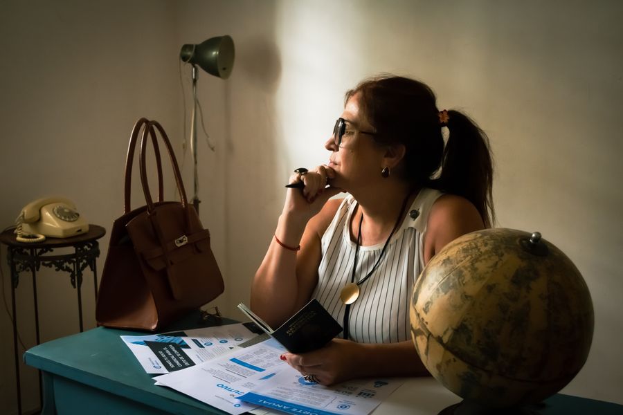 A woman in a home office, contemplating travel with documents and a globe.
