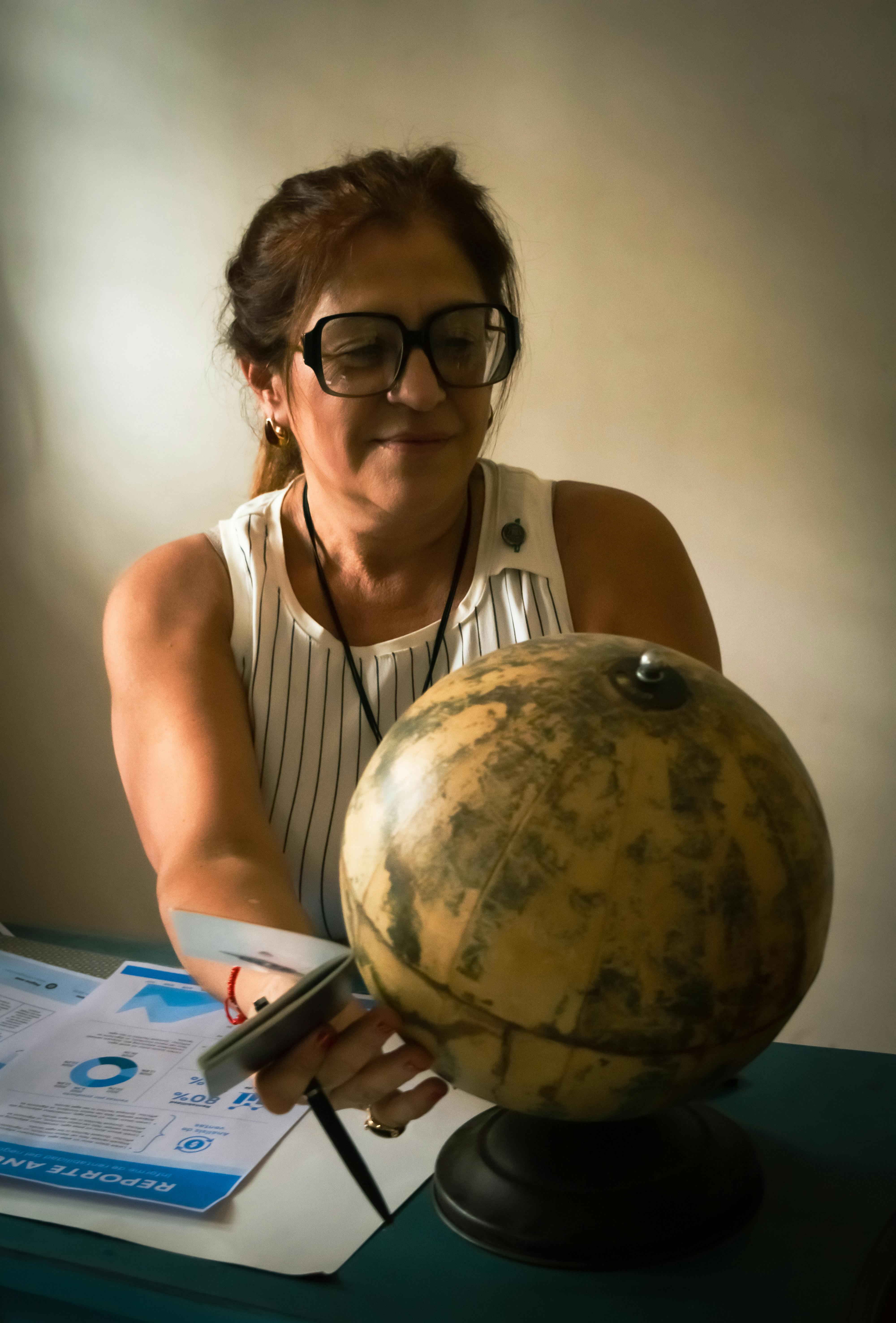 ฟรี ภาพหญิงคนหนึ่งในสำนักงานกำลังตรวจสอบลูกโลก เน้นย้ำถึงการศึกษาและการสำรวจ คลังภาพถ่าย