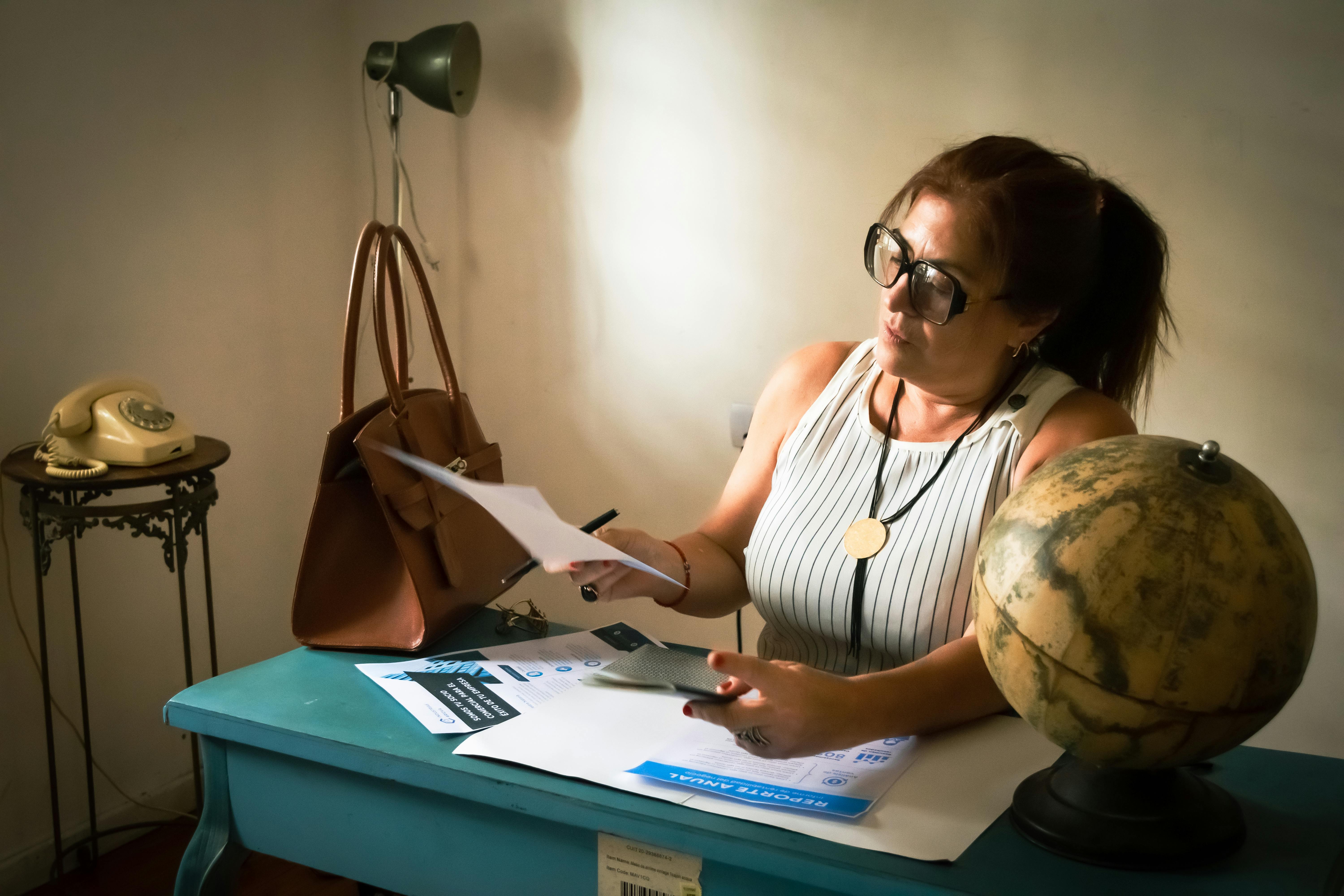Woman analyzes documents at a vintage desk with a globe, creating a cozy workspace ambiance.