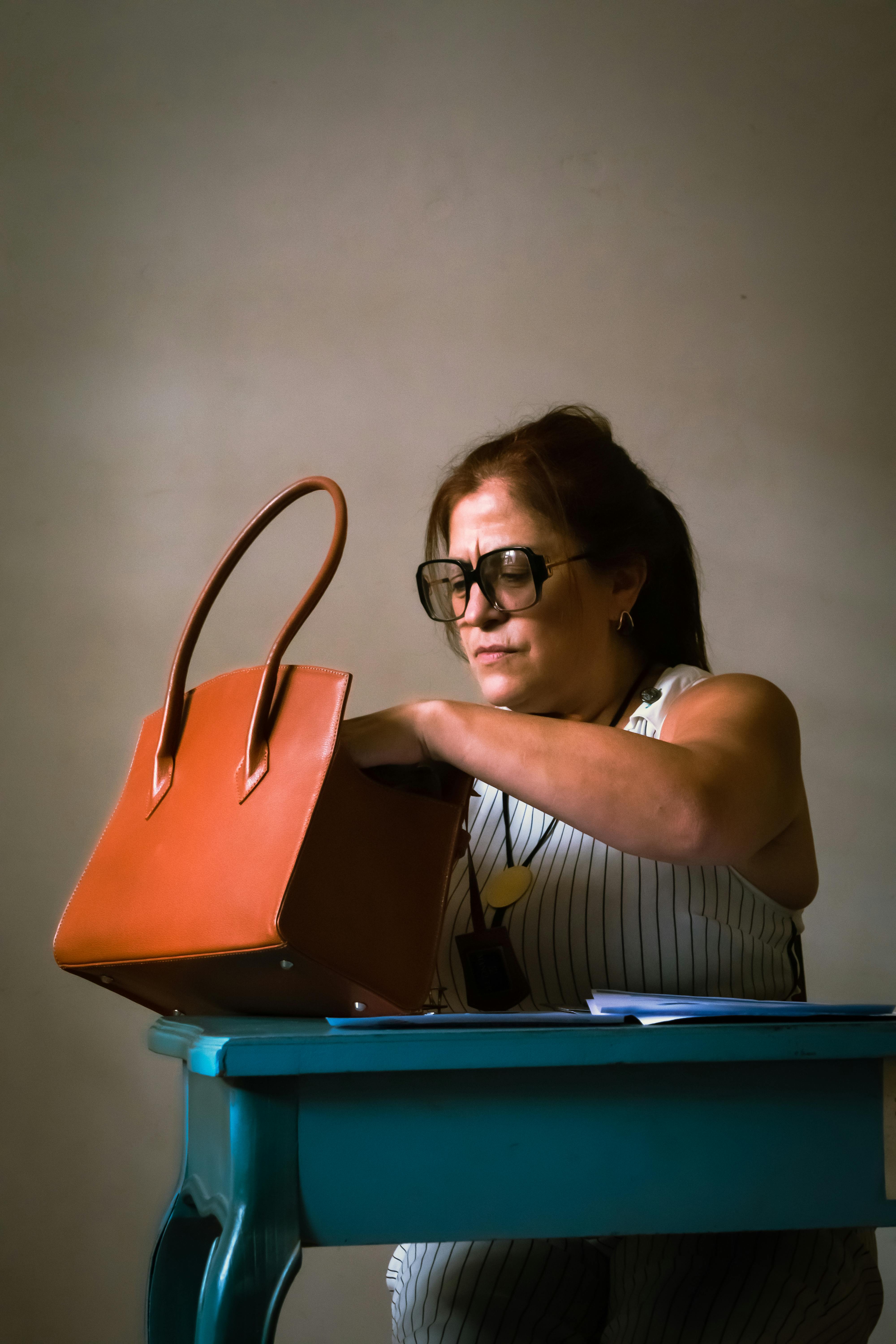 Безкоштовне Доросла жінка шукає в сумочці за синім столом з нейтральним фоном. стокове фото