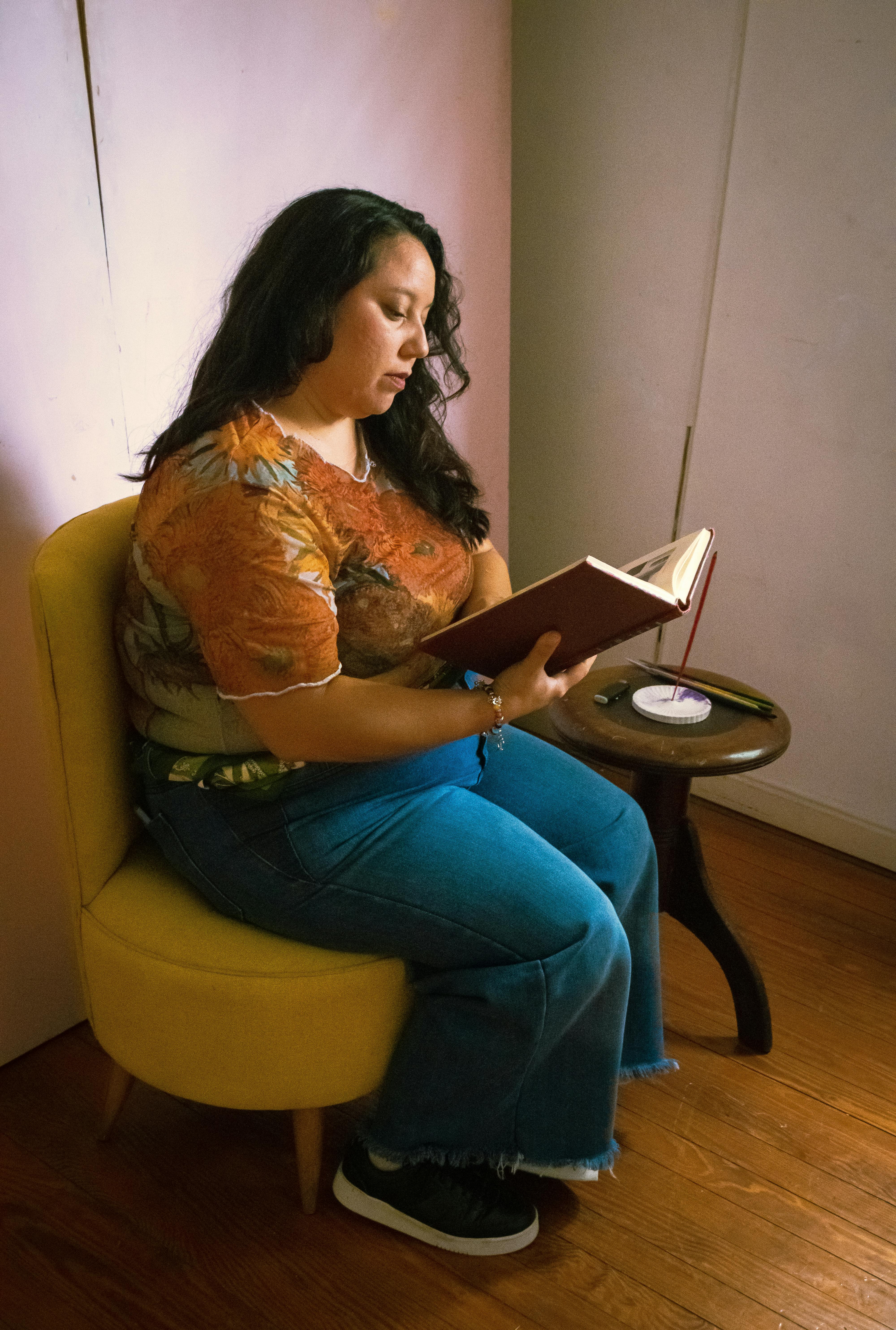 Безкоштовне Жінка сидить на жовтому стільці, читаючи книгу в приміщенні з задумливою зосередженістю. стокове фото